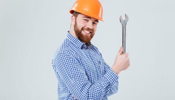 Smiling bearded young man in helmet with wrench