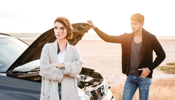 Young couple standing near broken car with open hood outdoors
